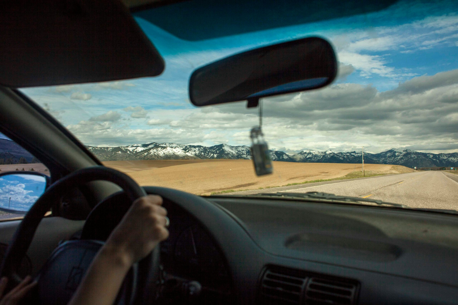 a view out the front window of a car, form the passenger side. The mountains are visible, and there are big white and gray clouds in a blue sky